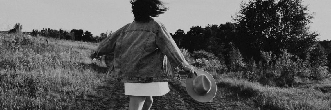 A young girl twirls joyfully outdoors on a sunny day, captured in black and white.